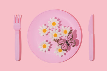 Spring creative layout with pastel pink plate, fork,knife, white flowers and butterfly on pastel pink background. 80s or 90s aesthetic fashion food restaurant concept. Minimal romantic summer idea.