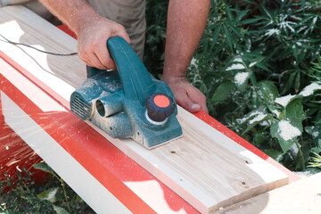 Electric tool planer working in the hands of a man. Professions, employment and work. DIY production by master carpenter, woodworking