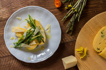 Rolled corn porridge with asparagus and cheese flakes on white plate and dark wood background