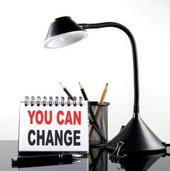 YOU CAN CHANGE text on notebook with pen and table lamp on the black background