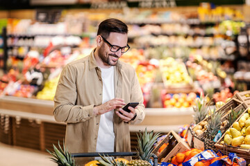 A man looking at the shopping list on the phone and purchasing at supermarket. - obrazy, fototapety, plakaty