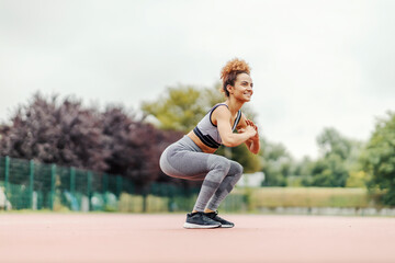 A fit sportswoman is doing squats endurance in the stadium in rainy weather. 