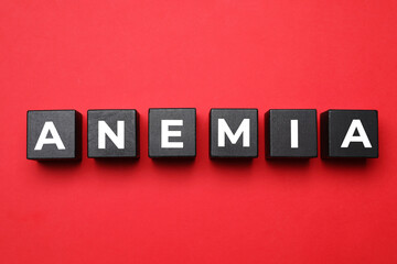 Wooden cubes with word Anemia on red background, flat lay