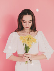 Woman model appearance holds in her hands yellow flowers on a pink background