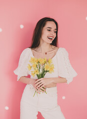 
Woman of model appearance holds yellow flowers in her hands and smiles on a pink background