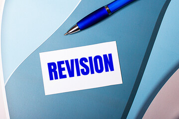 White blank card with REVISION text and blue pen on blue, cyan and pink background.