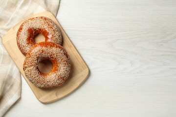 Delicious fresh bagels with sesame seeds on white wooden table, top view. Space for text