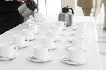 Waitress pouring hot drink during coffee break, focus on table with cups