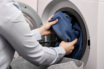Woman in light-colored shirt pulls dirty denim out soft basket and puts them in drum of washing...