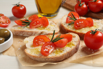 Tasty bruschettas with oil, tomatoes and rosemary on parchment paper, closeup