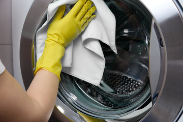 Carefully to shine woman's gloved hand rubs silver edge of washing machine door while cleaning...