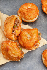 South African vetkoek, deep fried savory dough filled with saucy savory mince on mottled grey background with copy space

