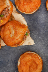South African vetkoek, deep fried savory dough filled with saucy savory mince on mottled grey...