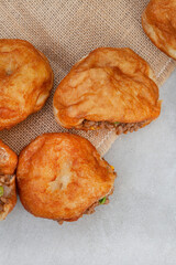 South African vetkoek, deep fried savory dough filled with saucy savory mince on mottled grey...