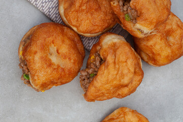 South African vetkoek, deep fried savory dough filled with saucy savory mince on mottled grey...