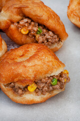 South African vetkoek, deep fried savory dough filled with saucy savory mince on mottled grey...