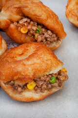 South African vetkoek, deep fried savory dough filled with saucy savory mince on mottled grey background with copy space

