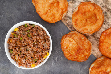 South African vetkoek, deep fried savory dough filled with saucy savory mince on mottled grey...