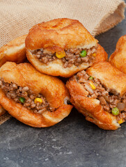 South African vetkoek, deep fried savory dough filled with saucy savory mince on mottled grey...