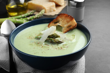 Bowl of delicious asparagus soup served on dark table, closeup