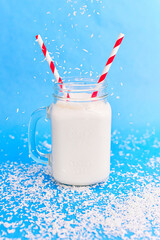 Blue background with the coconut falling into the glass of milk  with red and white straw