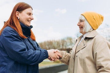 Two women friends or female partners meet on sity street. Successful business. Handshake of two business women on the background of modern buildings, partnership concept, Shaking hands to seal a deal