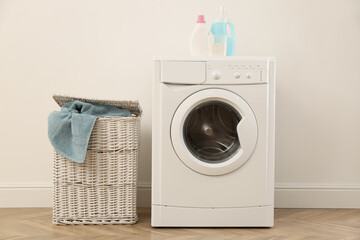 Laundry room interior with modern washing machine and wicker basket near white wall