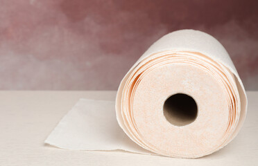 Roll of paper towels on white wooden table near pink wall, closeup. Space for text