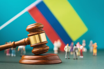 Judge gavel against the background of a blurred Colombian flag and plastic toy men, Colombian society litigation concept - obrazy, fototapety, plakaty