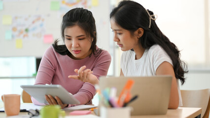 Two female colleagues examine the business marketing online survey result via tablet