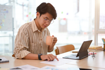 Focused Asian businessman sipping coffee while checking sale report