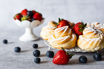 Delicious homemade profiteroles with powdered sugar, strawberries and blueberries. Gray background.