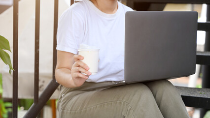 Fototapeta na wymiar Female sitting on the stairs, holding a coffee cup and using laptop.