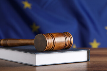Judge's gavel and book on wooden table against European Union flag, closeup