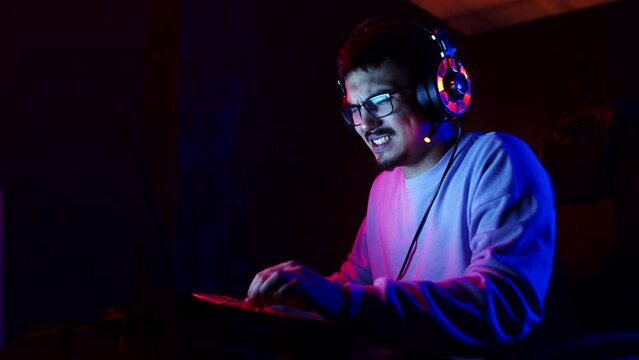 Young male gamer with headphones is playing videogames on laptop with an irritated and angry look, side view. Man is playing videogames on laptop. Concept of modern technologies