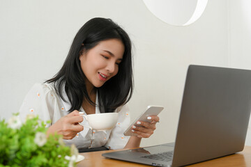 Female sitting at her workspace, sipping coffee and using her smartphone.