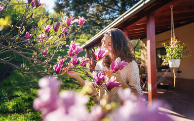 Young beautiful woman enjoying the spring of her home in the garden near a blooming magnolia tree...