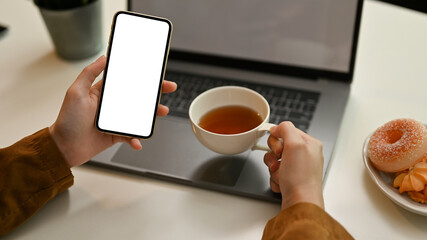 Female hands using a smartphone while sipping a cup of tea