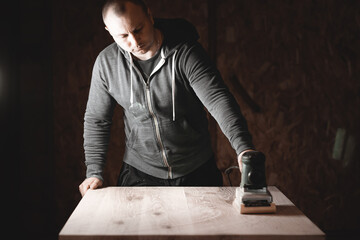A carpenter works in a workshop. Joiner's grinders, furniture manufacturing. A carpenter is grinding a wooden part with an electric sander.