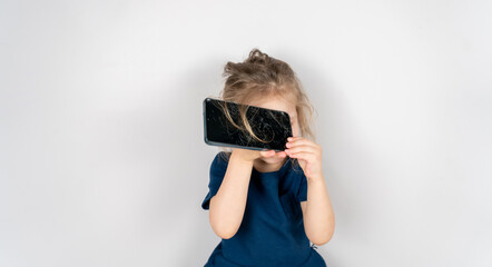 Portrait of terrified child with damaged phone. Upset little girl breaks screen of mobile phone. Kid girl holding broken display. Worried child accidentally destroyed smartphone