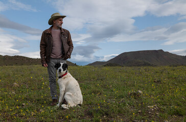 Adult man in cowboy hat and his dog standing on field against sky