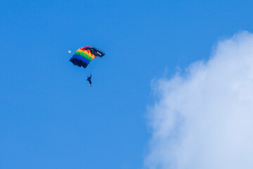 Naklejka na ściany i meble Pilot is paragliding with rainbow glide to promote lgbtq in gender equality in the extreme sport with bright blue sky and white fluffy cloud