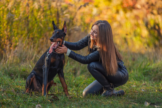 girl sitting near a doberman dog breed in nature