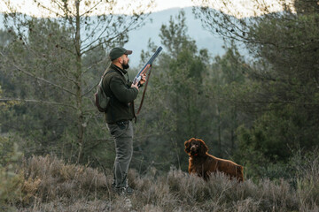 Standing hunter alert with his gun raised along with his dog