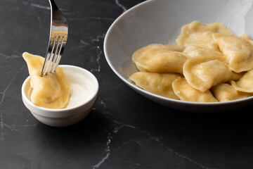 Isolated traditional ukrainian dish vareniki dipping in sour cream on black background. Menu or cook book concept