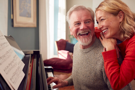 Smiling Senior Couple At Home Enjoying Learning To Play Piano