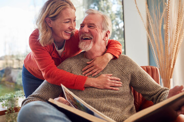 Smiling Senior Couple At Home Enjoying Looking Through Photo Album Together