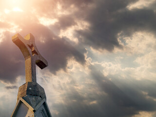Stone cross on a top of a church, dramatic cloudy sky in the background. Catholic religion symbol.