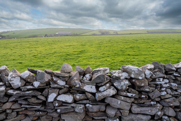 Traditional dry stone fence and big green grass field in Ireland. Blue cloudy sky. Simple rural...