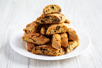 Homemade Italian Cantuccini with Chocolate on a White Plate on a white wooden surface, side view. Crispy Chocolate Cookies.